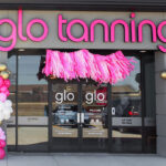 A storefront with pink "glo tanning" signage, pink and gold balloon garlands on either side of the glass doors.