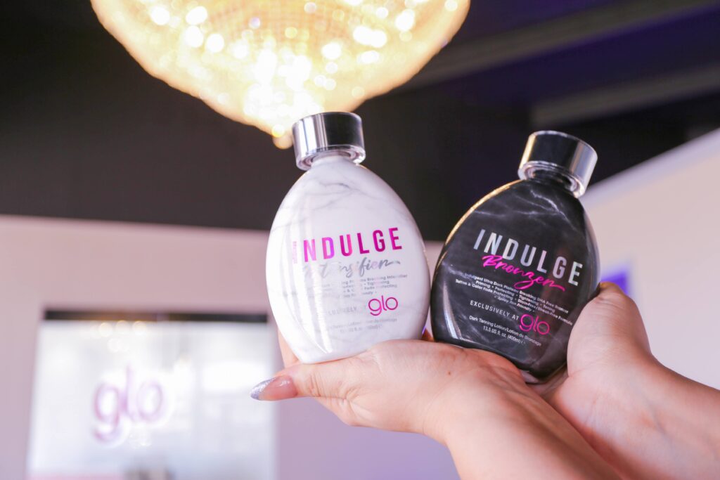 A woman's hands hold two tanning product bottles – Indulge bronzer and intensifier.